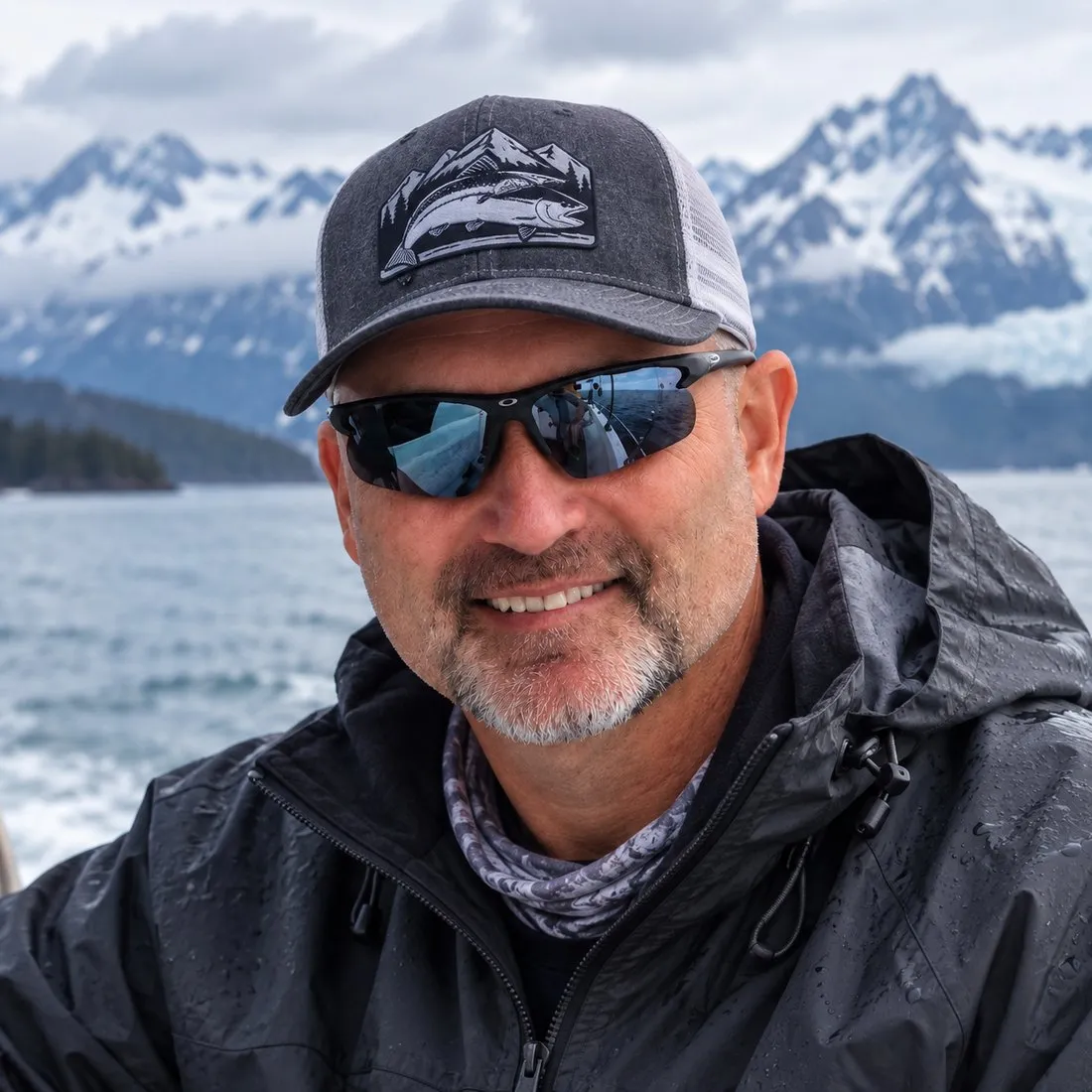 Bryan Collins on a boat in Alaska, snow-covered peaks and a glacier behind him