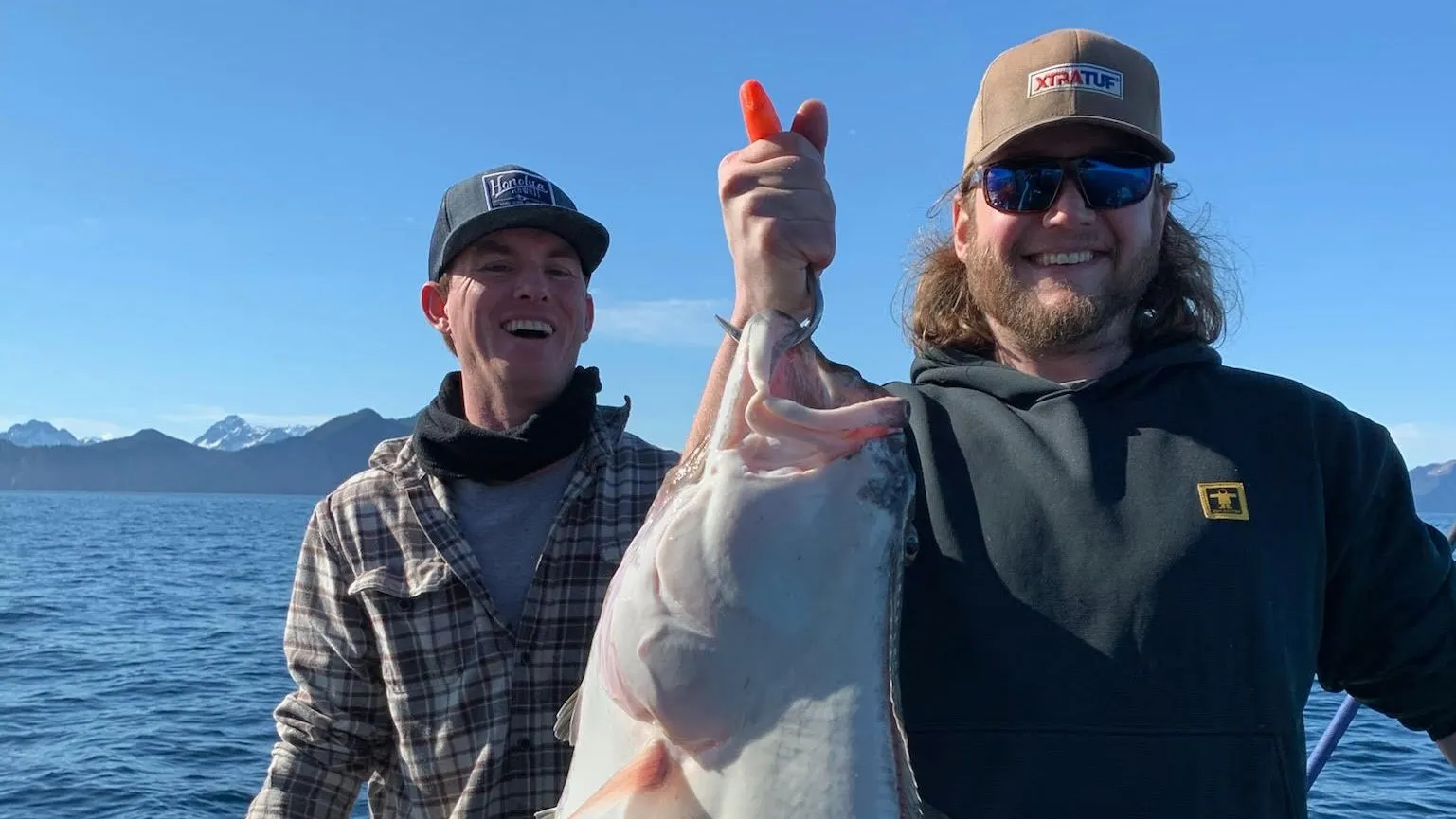 Two anglers on a charter boat holding up a Pacific halibut
